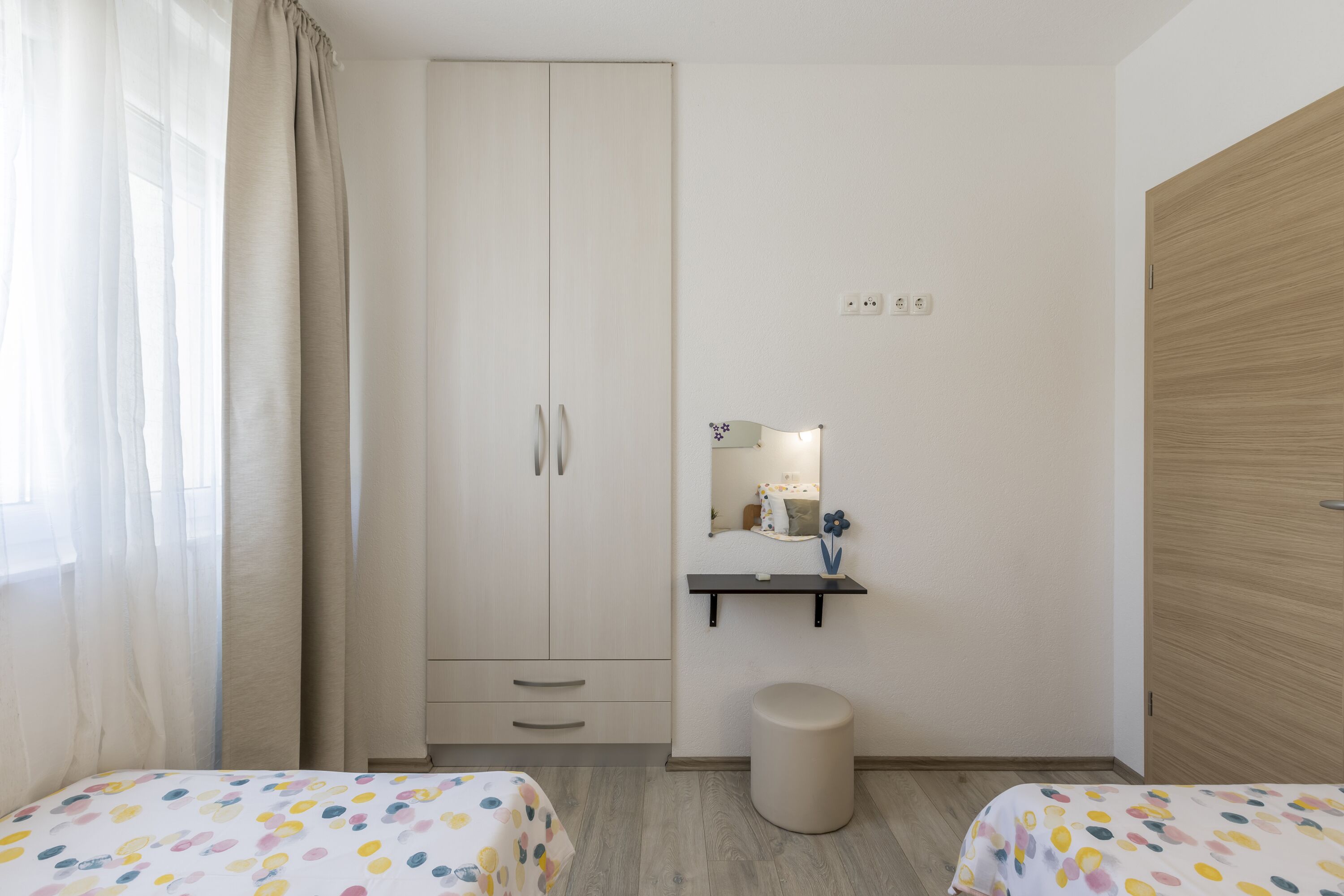 A bedroom with two beds, a wardrobe, a mirror, and a small shelf.