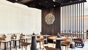 Un comedor moderno con mesas redondas y taburetes altos, con una pared decorativa central y un separador de madera.