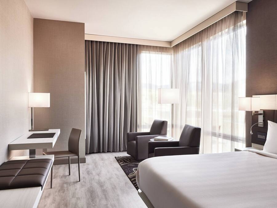 Ein modernes Hotelzimmer mit einem großen Bett, einem Schreibtisch mit Stuhl, einem kleinen Tisch mit Sitzgelegenheit und einem Sofa.