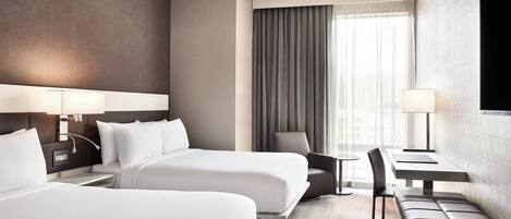 A hotel room with two beds, a desk, a chair, and a bench.