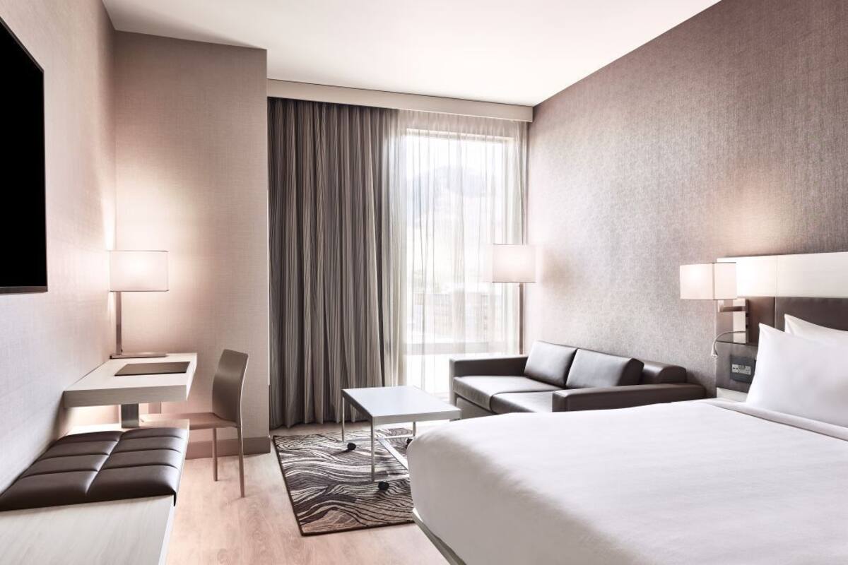 A modern hotel room with a large bed, a sofa, a desk, and a chair.