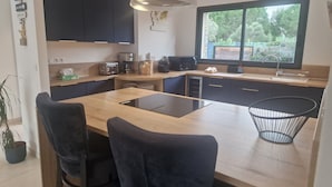 Ett modernt kök med en central köksö, svarta skåp och ett stort fönster med utsikt över grönområden.