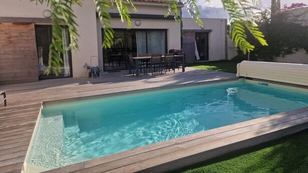 Ett modernt hus med en swimmingpool, utemöbler och en täckt uteplats.