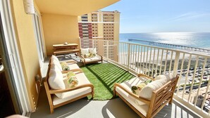 A balcony with a view of the ocean, a wooden sofa, a small table, and a chair. - Flip Flop at Calypso III. Luxury, view, location and amenities. Sleeps 9 (Panama City Beach)