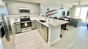 A modern kitchen with stainless steel appliances, a central island, and a dining area with a sofa and TV. - Flip Flop at Calypso III. Luxury, view, location and amenities. Sleeps 9 (Panama City Beach)