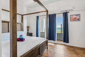 Een hemelbed met uitzicht op een balkon, een klein nachtkastje en een wandairconditioning.