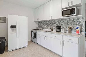 A modern kitchen with white cabinets, a built-in microwave, a gas stove, and a coffee maker.