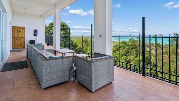 A covered balcony with wicker furniture, a wooden door, and a view of the ocean. - 3 Villas with Ocean Views & 2 Private Pools (Luquillo)