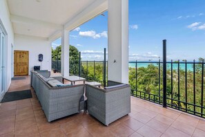 Un balcón techado con mobiliario de mimbre, una puerta de madera y vista al océano.