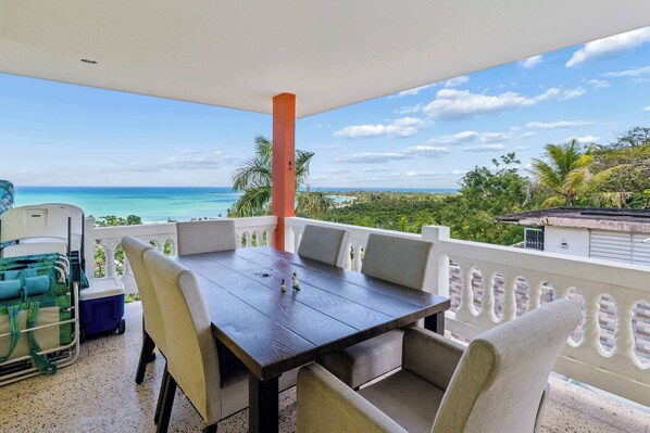 A balcony with a table and chairs, overlooking a beach and ocean.