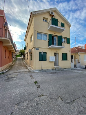 A multi-story building with a balcony, a street in front, and a clear sky. - Lithostroto Suites (Kefalonia)
