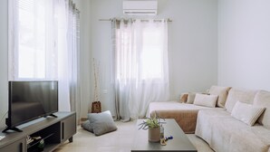 A modern living room with a flat-screen TV, a sofa, a coffee table with a plant, and sheer curtains. - Lithostroto Suites (Kefalonia)