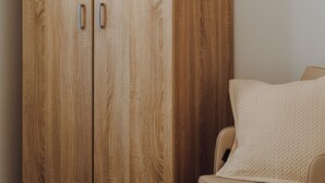 A wooden wardrobe with two doors and a chair with a cushion. - Lithostroto Suites (Kefalonia)