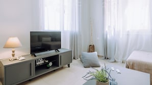 A modern living room with a flat-screen TV on a grey console, a white lamp, and a potted plant on a coffee table. - Lithostroto Suites (Kefalonia)