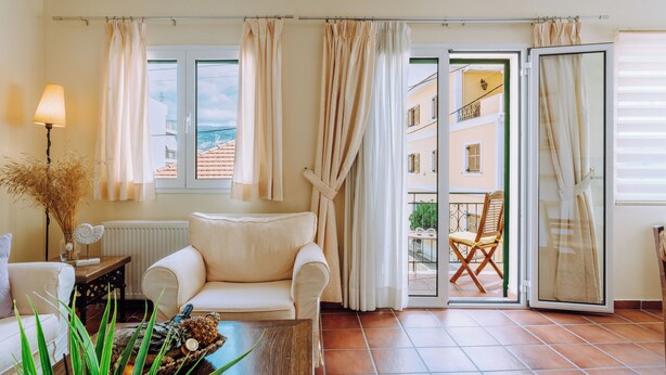 A living room with a sofa, a coffee table, and a view of a balcony with a chair. - Lithostroto Suites (Kefalonia)