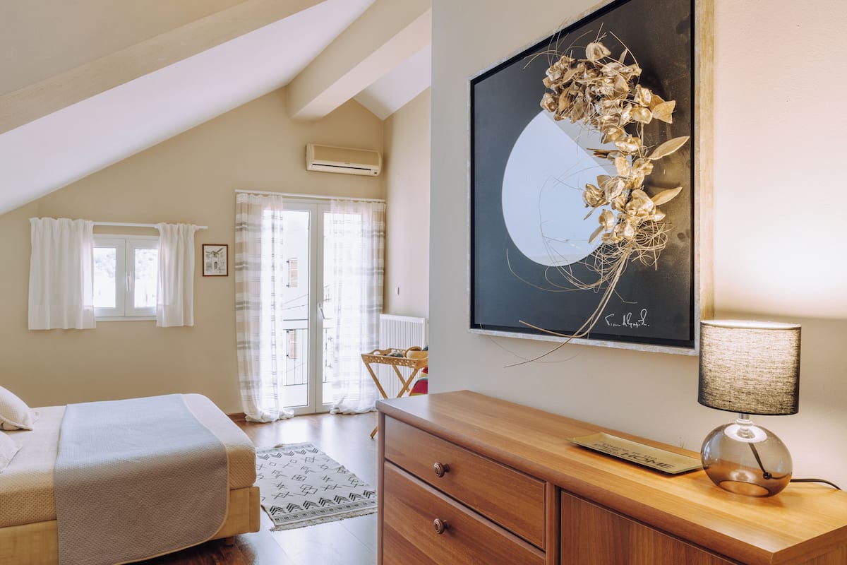 A bedroom with a bed, a dresser, a lamp, and a wall-mounted artwork.