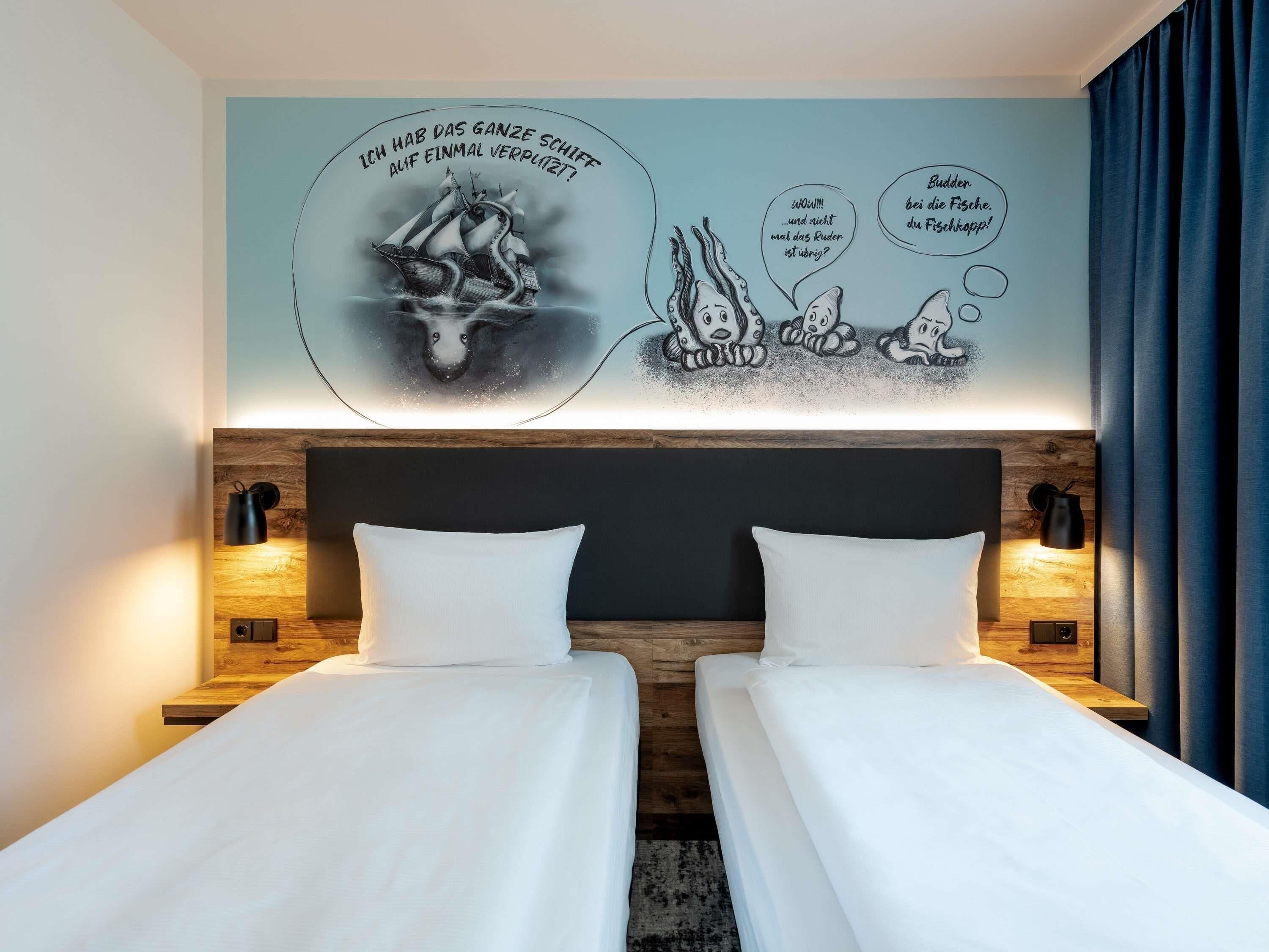 Habitación de hotel con dos camas, cabecero de madera y un mural en la pared.