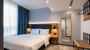 Een moderne hotelkamer met een bed, nachtkastje, spiegel en een klein houten bankje.