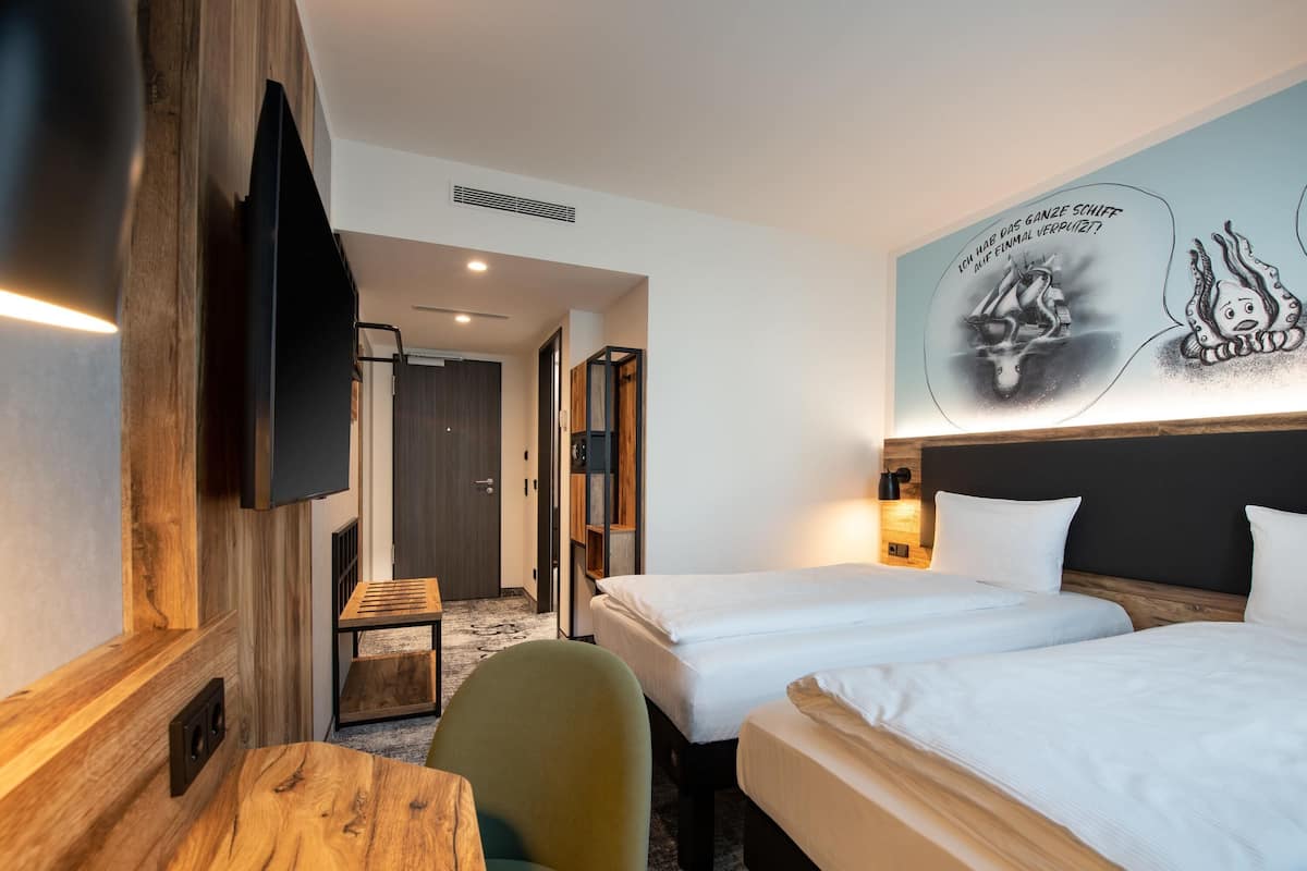 A hotel room with two beds, a desk, a chair, a TV, and a wall mural.