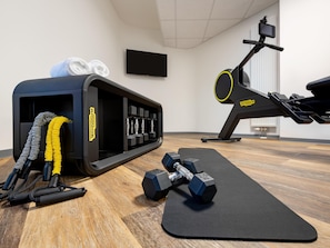 Une salle de sport équipée de matériel d’exercice, avec un tapis noir et un téléviseur fixé au mur.