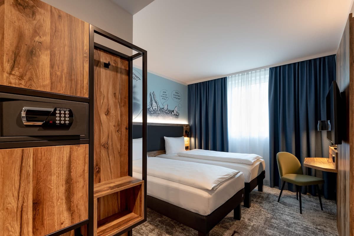 Een hotelkamer met twee bedden, een houten garderobe, een bureau met stoel, een televisie en een muur met een blauw gordijn.