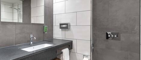 A modern bathroom with a grey and white tiled wall, a built-in sink, a toilet, and a mirror.