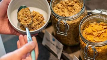 A person holding a bowl of cereal with a spoon, with jars of cereal in the background.