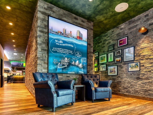 A lobby with a large TV screen, two leather armchairs, a stone wall, and framed pictures.