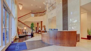 Um hall amplo com uma mesa de recepção, escadaria e um candelabro.