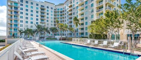 A hotel with a swimming pool, multiple balconies, and palm trees.