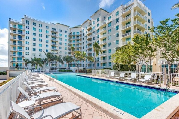 A hotel with a swimming pool, multiple balconies, and palm trees.