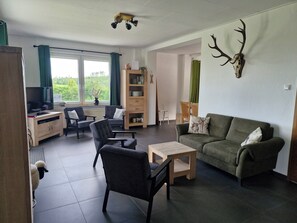 A living room with a sofa, chairs, a coffee table, a TV, a bookshelf, and a deer antler decoration. - Vacation home for up to 18 people with outdoor pool directly on the Aventura climbing mountain (Medebach)