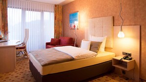 Habitación de hotel con cama, escritorio, silla, sofá rojo, un cuadro en la pared y una lámpara.