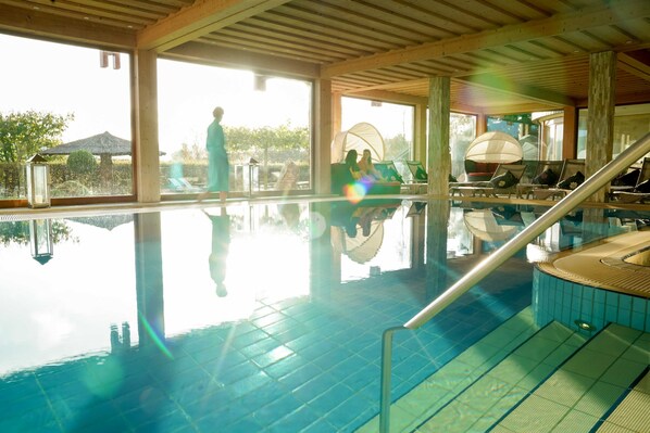 Une piscine intérieure à l’eau claire, avec un intérieur baigné de lumière et des chaises longues.