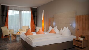 Ein modernes Hotelzimmer mit einem großen Bett, einer Sitzecke mit Tisch und Blick ins Freie durch große Fenster.
