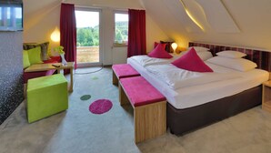 A modern bedroom with a large bed, two benches, a desk, and a TV. - Junior Suite - Hotel Freund (Vöhl)