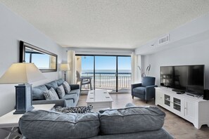 Relax in this stylish living room with a large flat-screen TV, comfortable sofa, and armchair, offering a view of the beach.