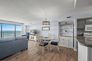 Enjoy a spacious living area with a sofa and dining table, kitchen with cabinetry and a small island, and a balcony with ocean views.