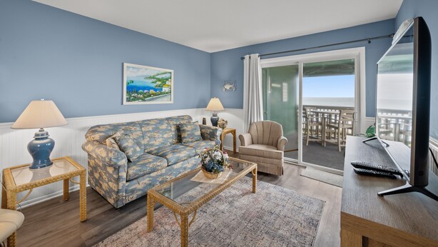 Un salon comprenant un canapé, un fauteuil, une table basse et un téléviseur. Il y a également un balcon avec vue.