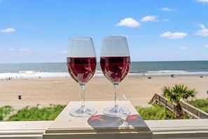 Duas taças de vinho sobre uma mesa, com vista para a praia.