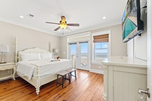 Une chambre à coucher comprenant un lit, une table de chevet, un banc, un ventilateur de plafond et un téléviseur.