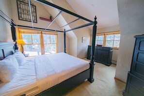 A bedroom with a four-poster bed, a dresser, and a window with a view of trees.