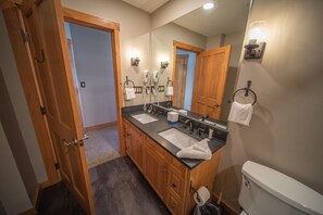 Bathroom features a double sink vanity with two faucets and soap dispensers, a toilet, and a towel rack.