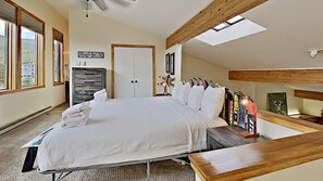 Une chambre avec un grand lit, une tête de lit en bois, un puits de lumière, une commode et un porte-skis fixé au mur.