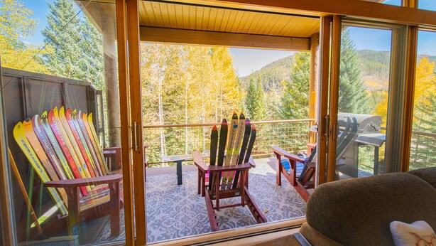 A room with a large window overlooking a forested area, a wooden chair, and a table.