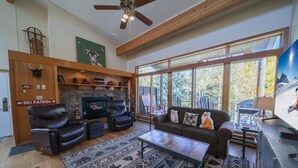 A spacious living room with a fireplace, leather sofas, a coffee table, and a large window offering a view of the outdoors.