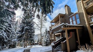 A snow-covered pathway leading to a lodge with a wooden staircase and a balcony.