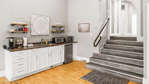 A modern kitchen with white cabinets, a granite countertop, and a stainless steel dishwasher. There are shelves with glassware and a microwave. A staircase with a metal railing leads to another level. - Tandem Suite - Spacious 2 Bedroom Suite Walkable to Downtown TC (Traverse City)
