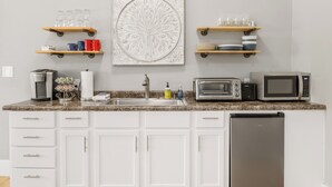 A kitchen with white cabinets, a granite countertop, a stainless steel refrigerator, a microwave, a toaster, and shelves with glassware and mugs. - Tandem Suite - Spacious 2 Bedroom Suite Walkable to Downtown TC (Traverse City)