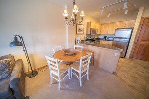 A compact kitchen with a dining area, wooden cabinets, stainless steel appliances, and a chandelier.